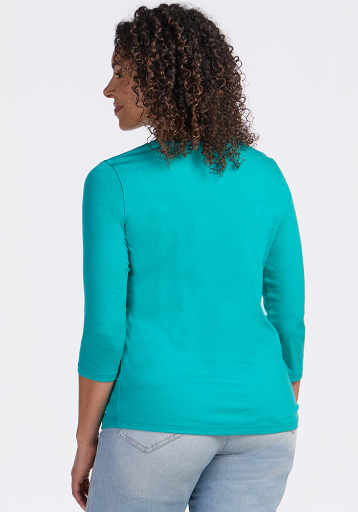 Woman with curly hair wears the Woolx Elena 3/4 Sleeve V Neck in Cool Jade and light blue jeans, shown from back.