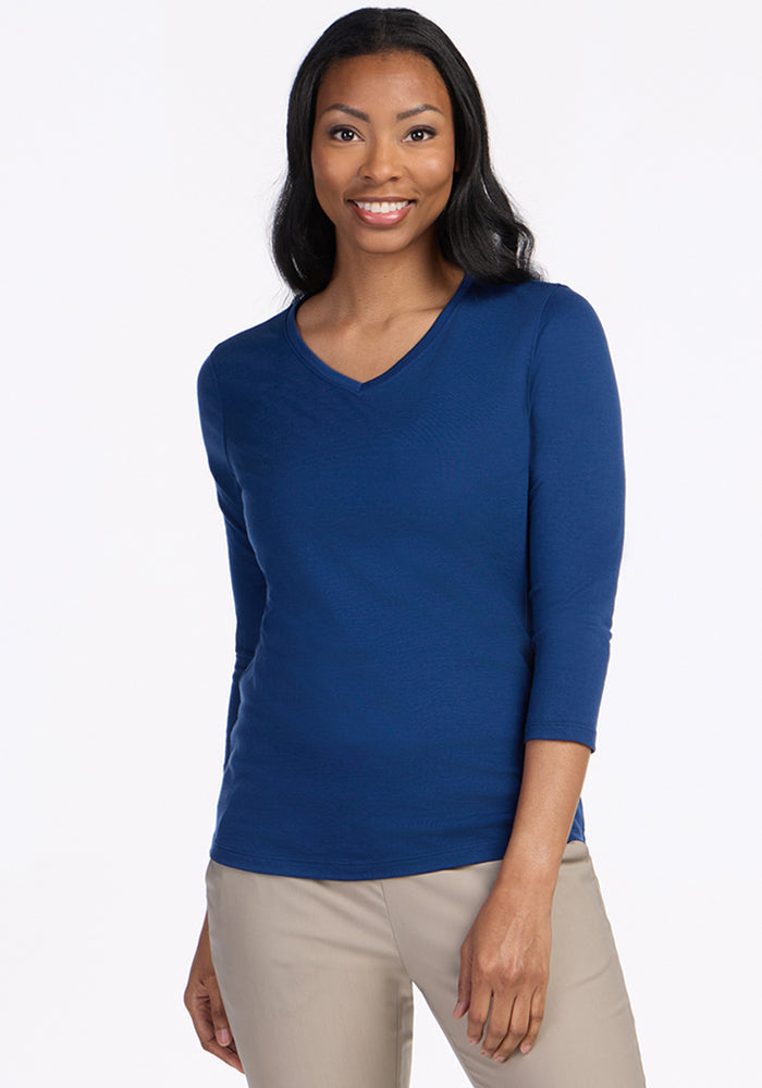 Smiling woman in Woolx Elena 3/4 Sleeve V Neck in Estate Blue and beige pants, against a plain white background.