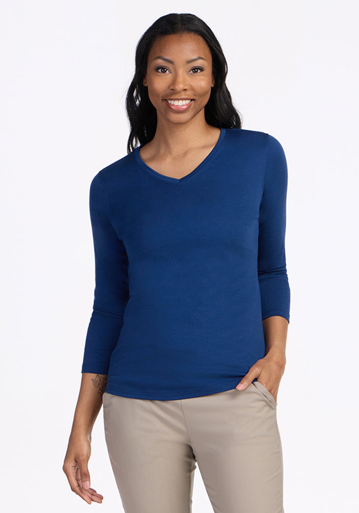 Woman smiling in a Woolx Elena 3/4 Sleeve V Neck, Estate Blue, final sale, with beige pants on a white background.