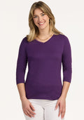 Smiling blonde woman wears Woolx Elena 3/4 Sleeve V Neck in Plum Crush and white pants, against a light background.