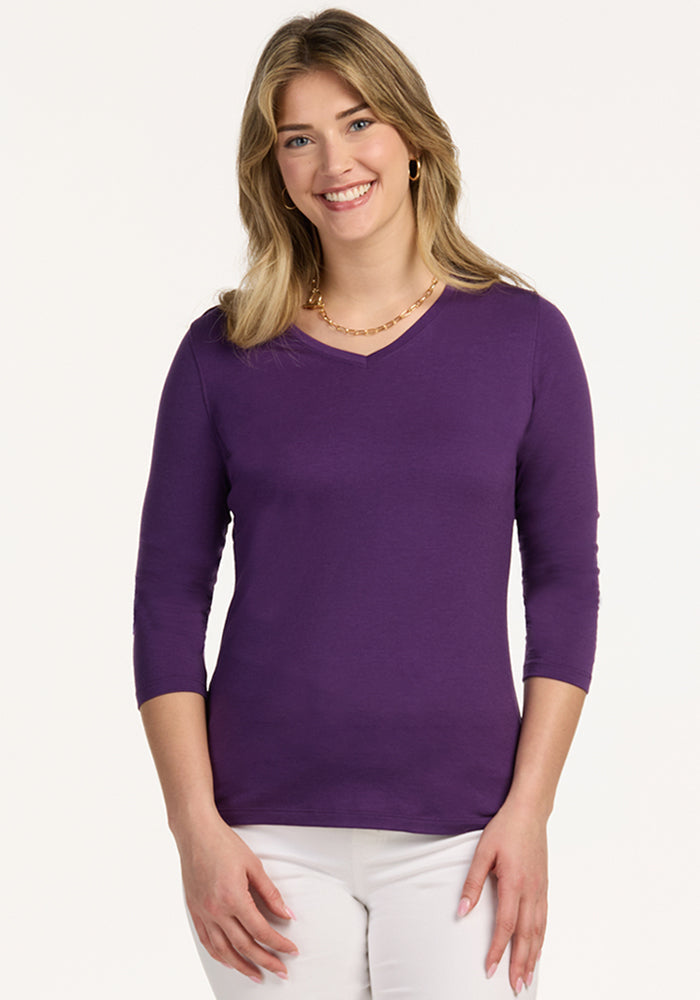 Smiling blonde woman wears Woolx Elena 3/4 Sleeve V Neck in Plum Crush and white pants, against a light background.
