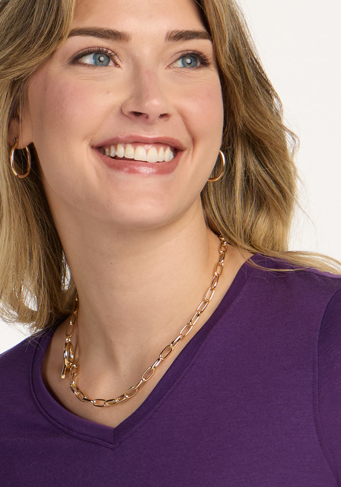 Smiling woman with blonde hair wearing a Woolx Elena 3/4 Sleeve V Neck in Plum Crush, gold hoops, and a chain necklace.