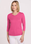 Woman wears the Woolx Elena 3/4 Sleeve V Neck in Raspberry Fizz with white pants, against a plain light background.