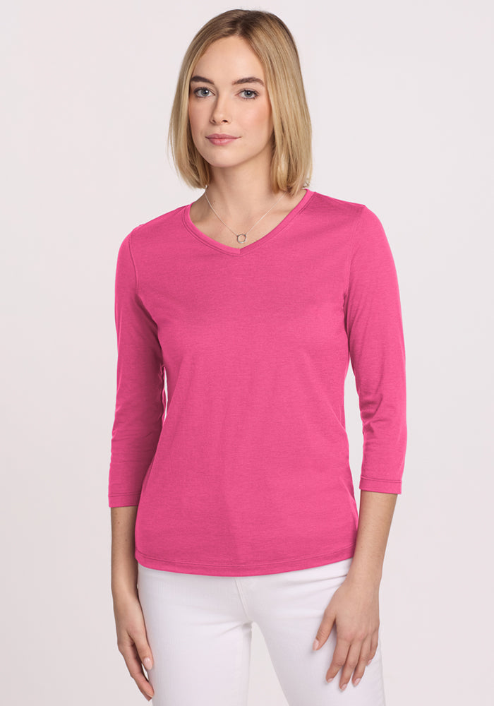 Woman wears the Woolx Elena 3/4 Sleeve V Neck in Raspberry Fizz with white pants, against a plain light background.