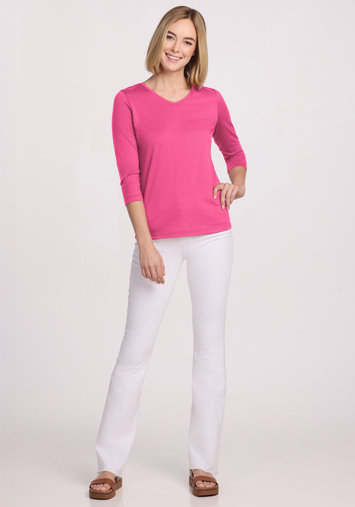Woman smiling in a Woolx Elena 3/4 Sleeve V Neck in Raspberry Fizz, white pants, and brown sandals.