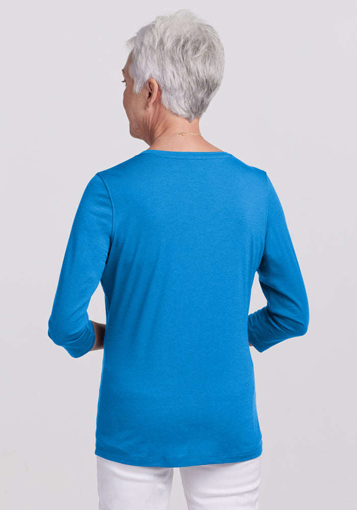 Older woman in a bright blue Woolx Elena 3/4 Sleeve V Neck (Wave Rider) and white pants, shown from the back.