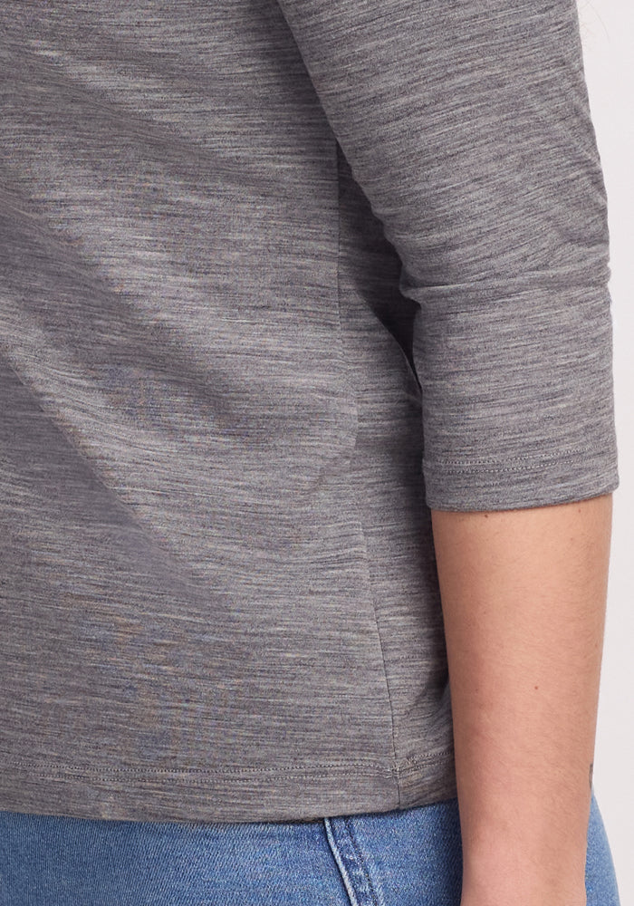 Close-up of a person in blue jeans, wearing the Woolx Elena 3/4 Sleeve V Neck in Graphite Heather. Their bent arm highlights the shirt's texture.