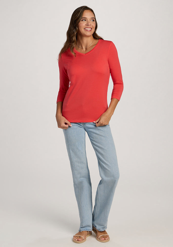 Woman in a Woolx Elena 3/4 Sleeve V Neck - Hibiscus, light blue jeans, and sandals, smiling against a plain background.
