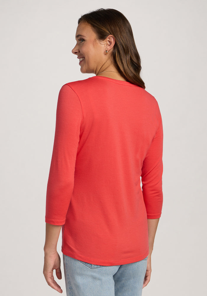 Woman smiling, facing away, in a Woolx Elena 3/4 Sleeve V Neck - Hibiscus and light blue jeans against a plain background.