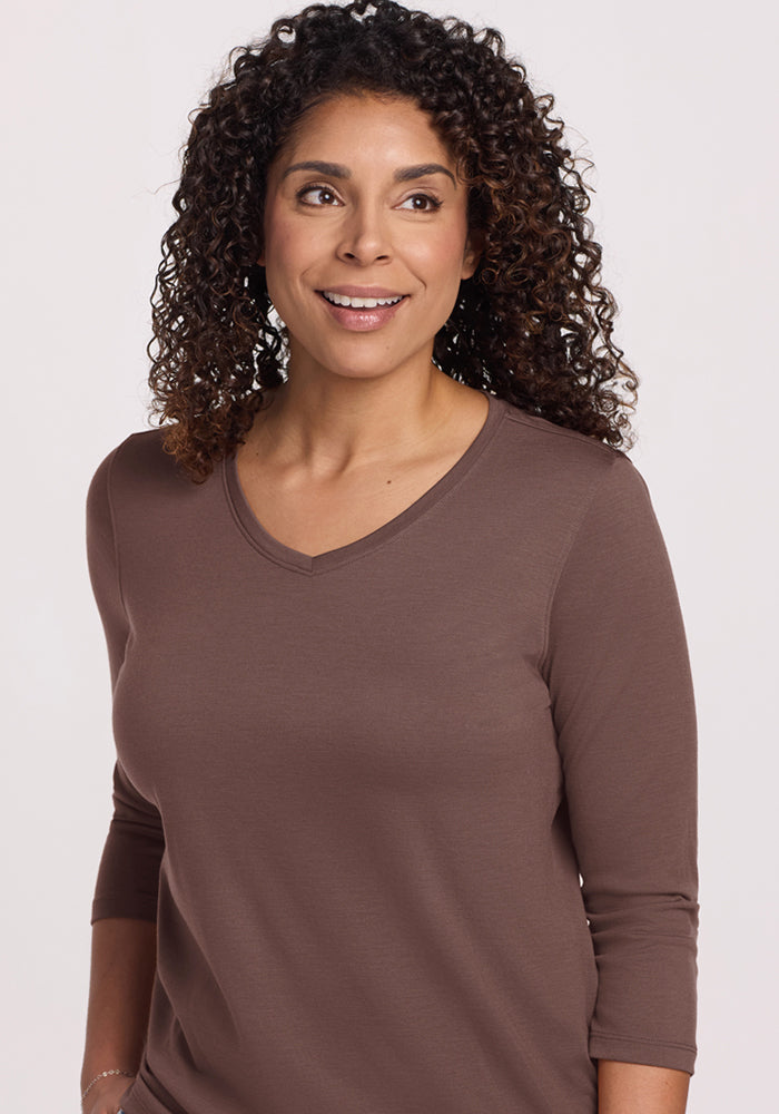 Woman with curly hair smiles, wearing the Woolx Elena 3/4 Sleeve V Neck in Peppercorn, looking to the side.