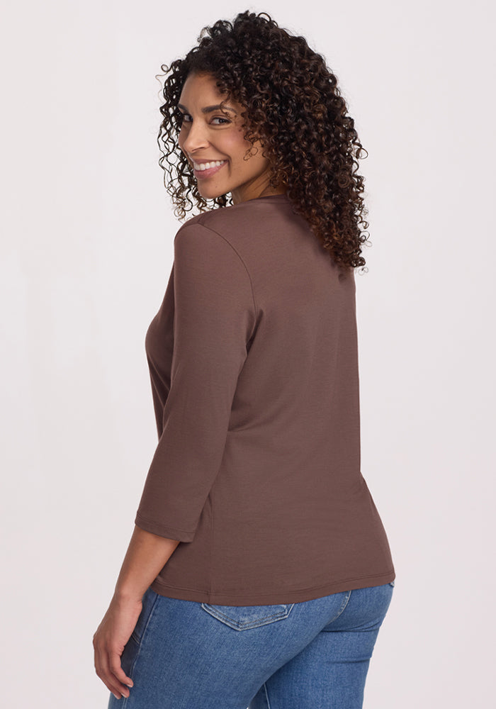 Smiling woman in a Woolx Elena 3/4 Sleeve V-Neck Peppercorn top and blue jeans, looking over her shoulder.