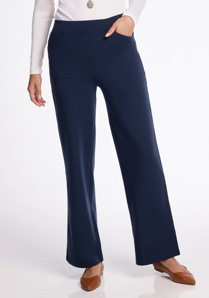 Someone is styled in a white long-sleeve top, paired with the Woolx Ellie Wide Leg Pants in Deep Navy and brown shoes. The striking wide-leg fit stands out against a plain white background, with only the lower half of the body visible. | Georgia is 5'10", wearing a size XS