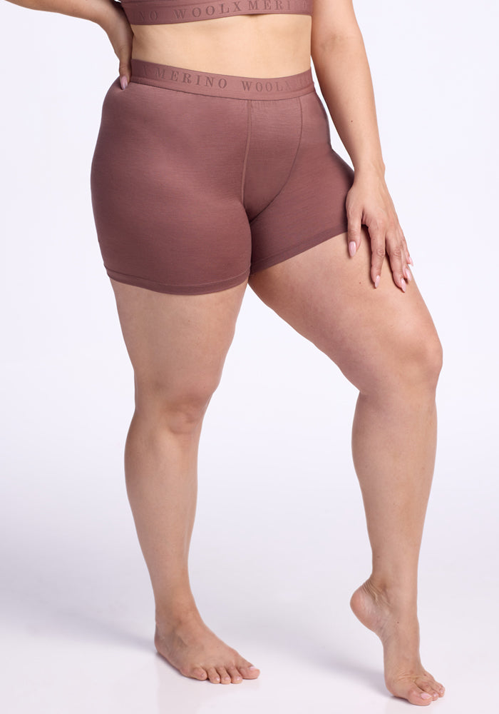 A person with medium skin tone wears the Woolx Elliott Boyshort in Nutmeg, paired with a matching top. Barefoot, they pose on one leg with a hand on their thigh against a plain white background. | Juliana is 5'10", wearing a size XL