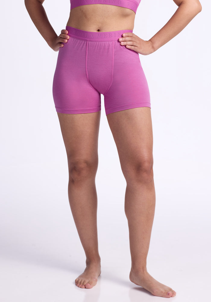 A person, shown from the shoulders down against a white background, models Woolx Elliott Boyshort - Wild Blossom: a quick-drying matching set of pink shorts and crop top. The person is barefoot with arms slightly bent. | Tori is 5'7", wearing a size S