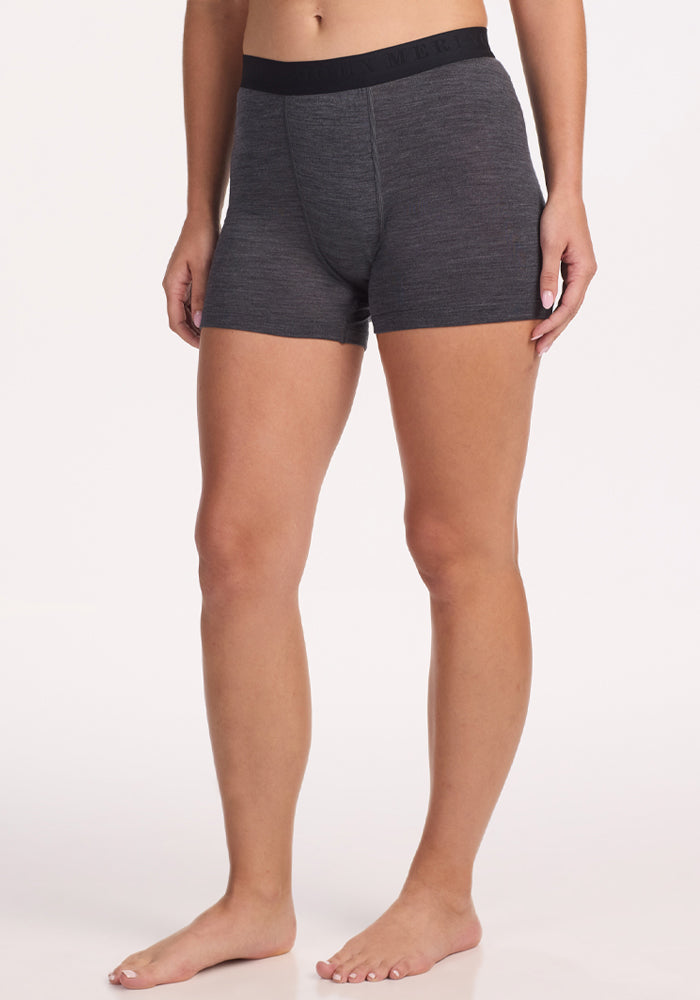 A person stands barefoot, wearing Woolx Elliott Boyshort in Cinder Melange with a black waistband, shown from mid-torso to feet against a plain white background. | Ariana is 5'11", wearing a size S
