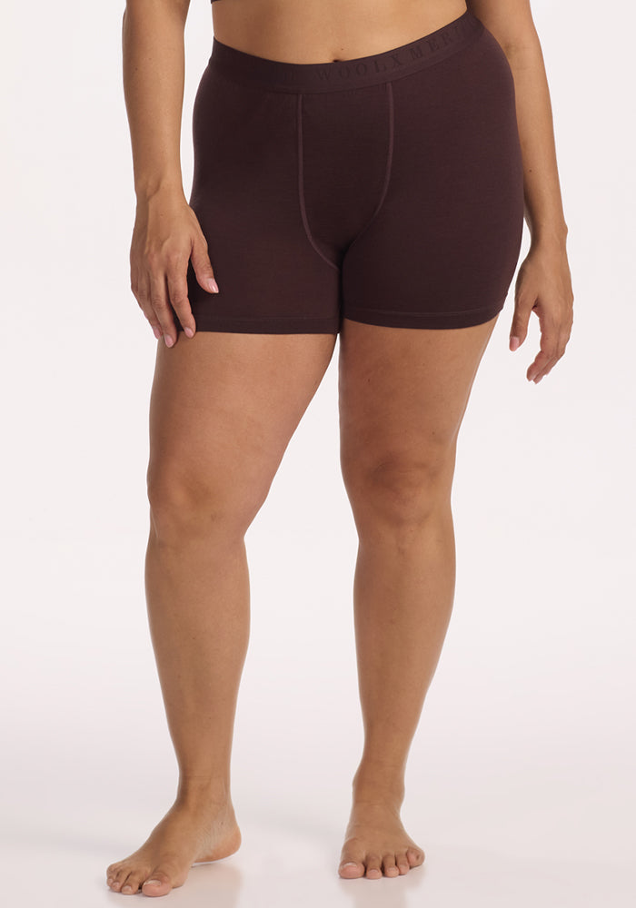 A person stands barefoot in Woolx Elliott Boyshort - Chocolate Plum, temperature-regulating underwear with an elastic waistband, against a plain white background. Their arms are relaxed by their sides. | Juliana is 5'10", wearing a size XL