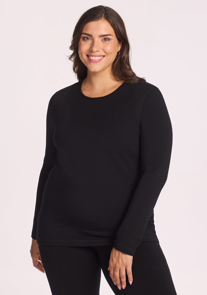 A smiling woman with medium-length brown hair models the Woolx Elsa Long Sleeve in black, paired with matching black pants, standing against a plain light background. | Juliana is 5'10", wearing a size XL