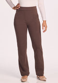 A person wears a long-sleeved white top, beige flats, and Woolx Emerson Straight Leg Pants Petite in Bracken, standing with one hand on their hip against a plain light background.