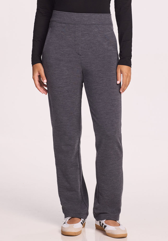 A person wears Woolx Emerson Straight Leg Pants in Cinder Melange, a long-sleeve black top, and white sneakers with black accents, standing against a plain light background. | Tori is 5'7", wearing a size S