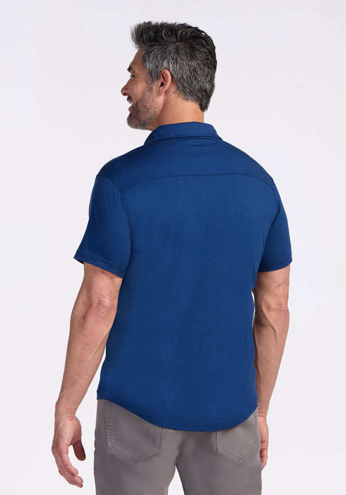 A man with short gray hair and a beard stands with his back to the camera, wearing the Woolx Endi Full Button Down Shirt in Estate Blue and light gray pants against a plain white background.