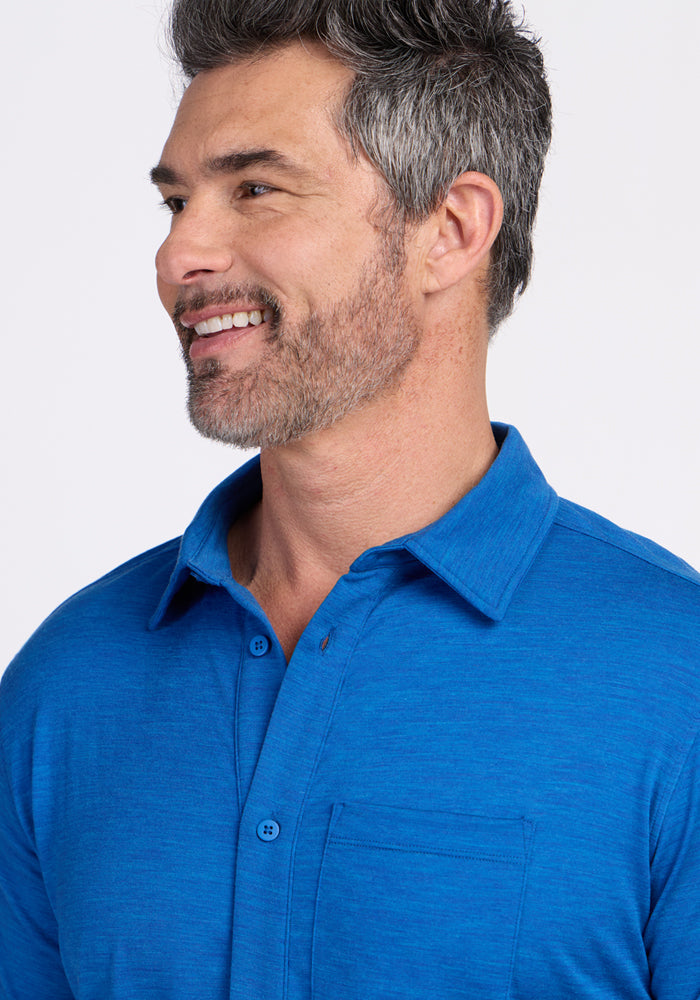 A smiling man with short gray hair and light stubble wears the Woolx Endi Full Button Down Shirt in Glacial Blue, shown from the chest up against a plain, light background.