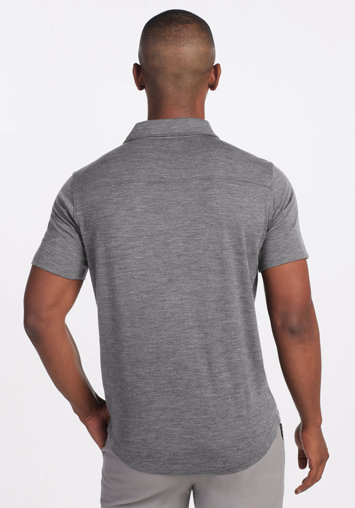 A man stands with his back to the camera, wearing the Woolx Endi Full Button Down Shirt in Graphite Heather and light gray pants, set against a plain white background.