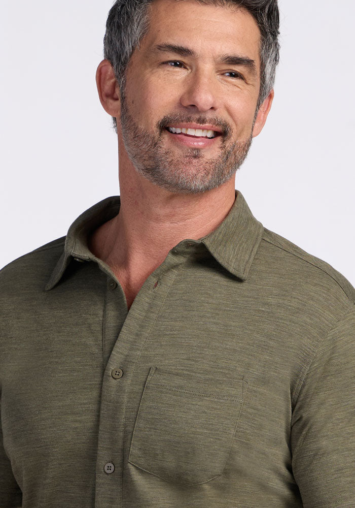 A middle-aged man with short gray hair and a beard smiles while wearing the Woolx Endi Full Button Down Shirt in Sage Olive Melange, a Merino wool collared shirt featuring a chest pocket.