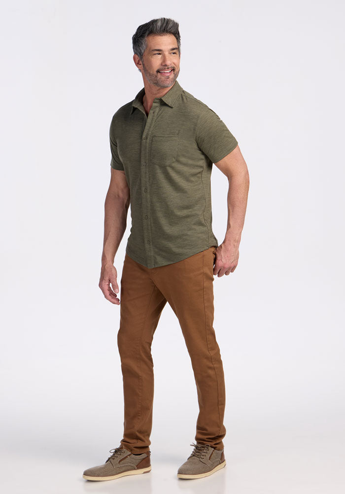 A gray-haired, bearded man stands smiling against a plain white background, wearing the Woolx Endi Full Button Down Shirt in Sage Olive Melange, brown pants, and tan shoes.