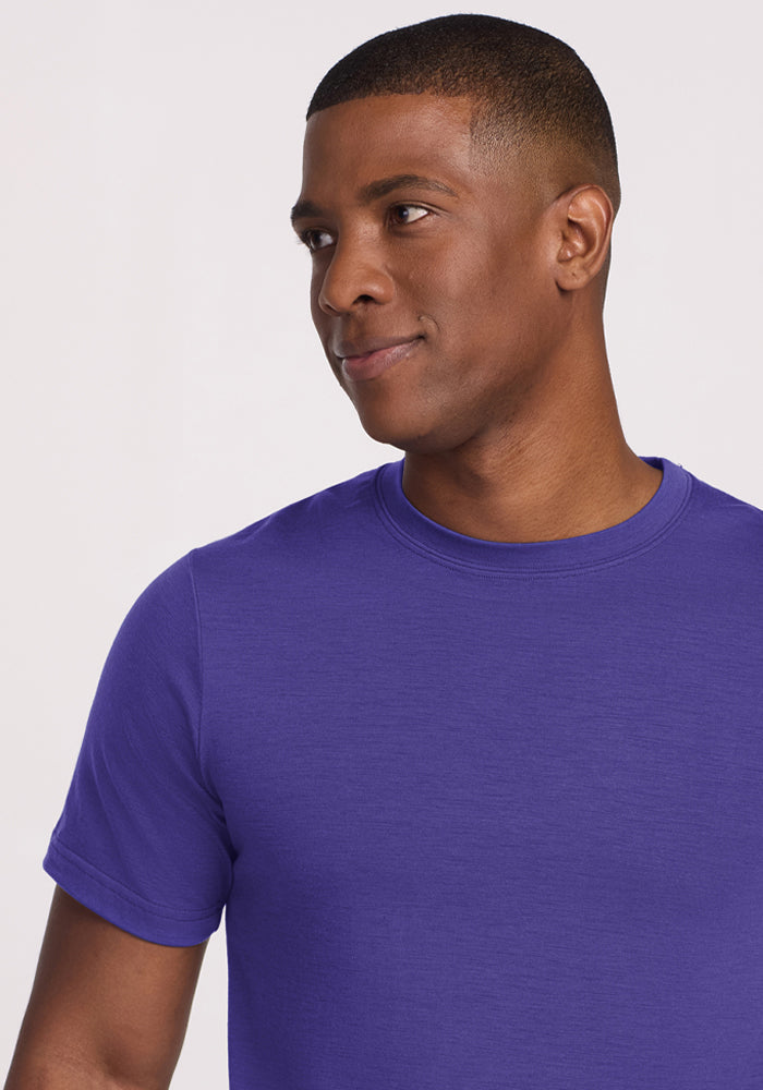 Man wears Woolx Endurance Tee in Berry Indigo, smiling softly and looking slightly to the side against a light backdrop.