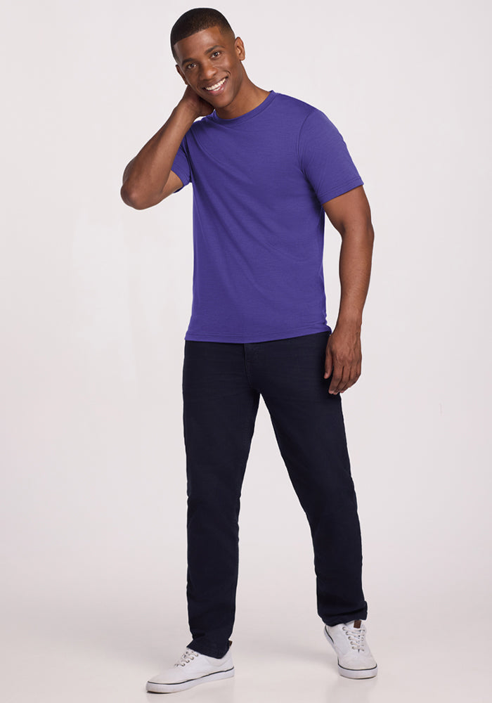 Smiling man in Woolx Endurance Tee - Berry Indigo, dark pants, and white sneakers stands touching his neck.