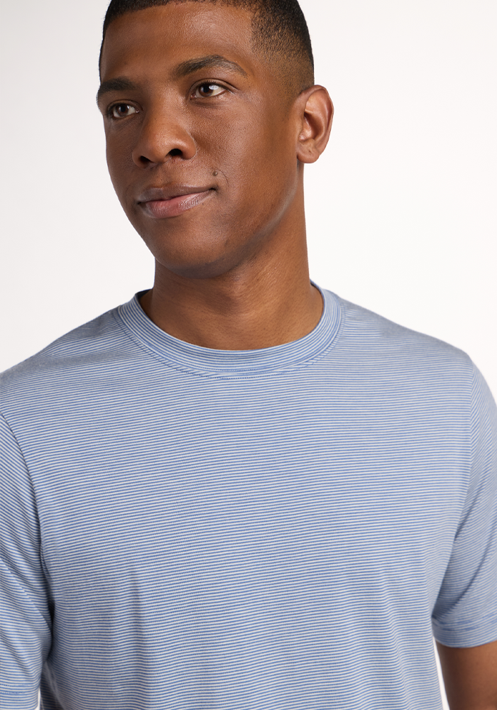 A young man with short hair wears the Woolx Endurance Tee in Blue Sand Mini Stripe and looks slightly to the side with a neutral expression against a plain, light background.