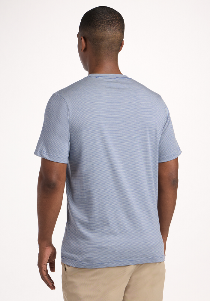 A man faces away from the camera wearing a Woolx Endurance Tee - Blue Sand Mini Stripe and beige pants—perfect travel performance gear—set against a plain white background.