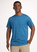 Man wearing a Woolx Endurance Tee - Coastal Mini Stripe and beige pants, smiling against a plain light background. | Trell is 6’2”, wearing a size M