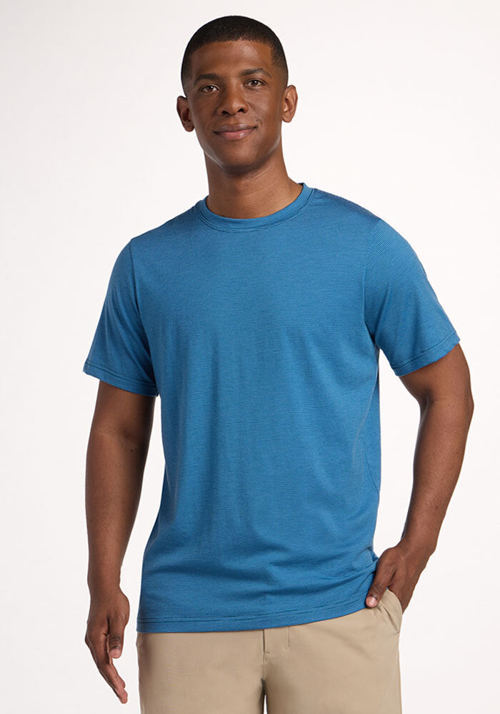 Man wearing a Woolx Endurance Tee - Coastal Mini Stripe and beige pants, smiling against a plain light background. | Trell is 6’2”, wearing a size M