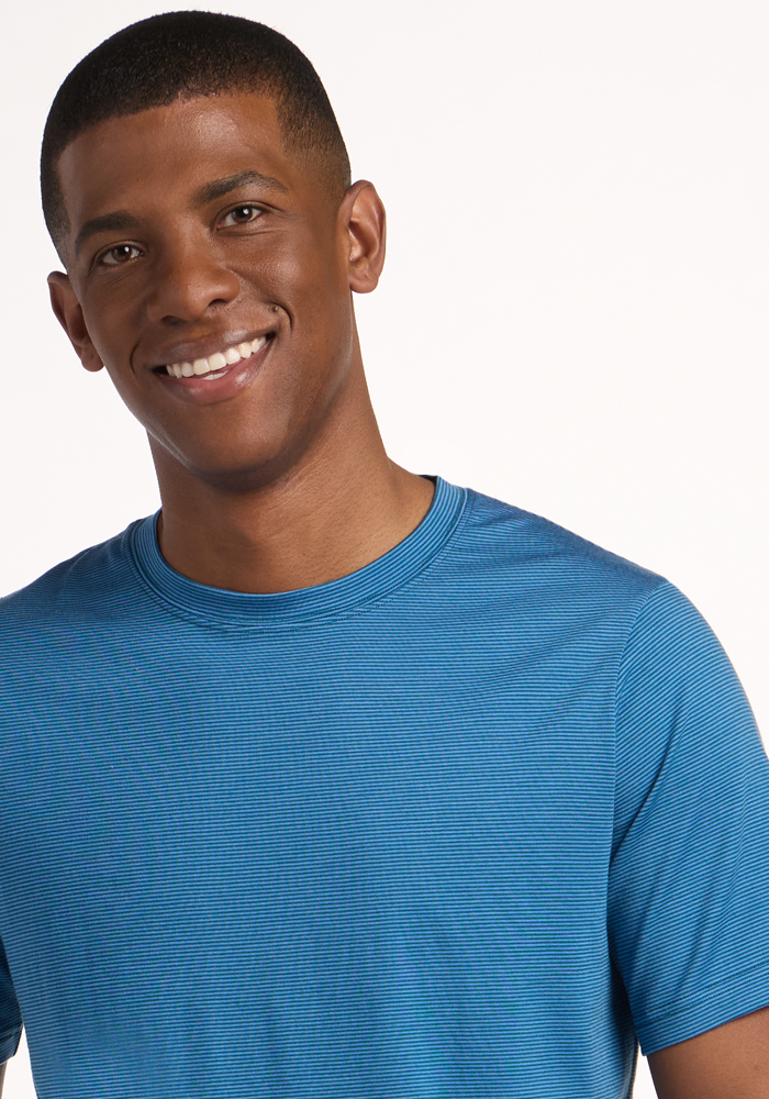 A man wearing a Woolx Endurance Tee - Coastal Mini Stripe smiles at the camera against a plain, light background.