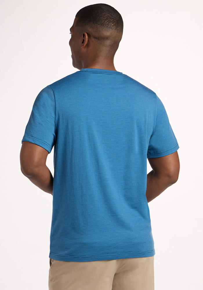 A man stands with his back to the camera, wearing the Woolx Endurance Tee - Coastal Mini Stripe and beige pants against a plain light background.