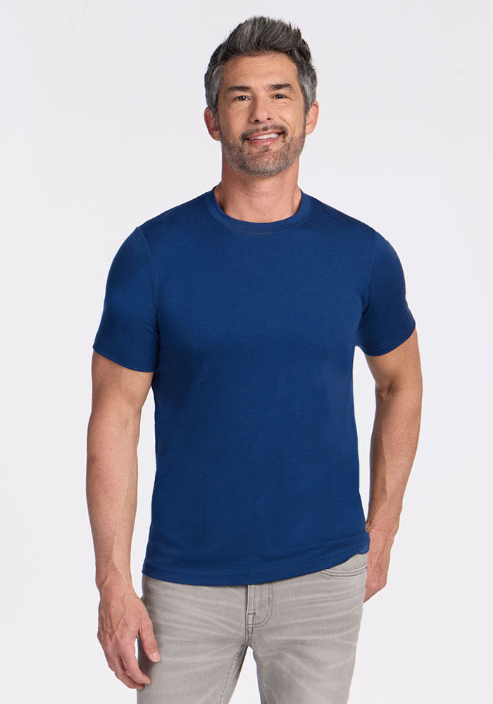 A man with short gray hair smiles in a Woolx Endurance Tee in Estate Blue and light gray jeans against a white background.