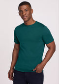 Man wearing a Woolx Endurance Tee in Riverbank Green and black pants, standing against a plain background, smiling.