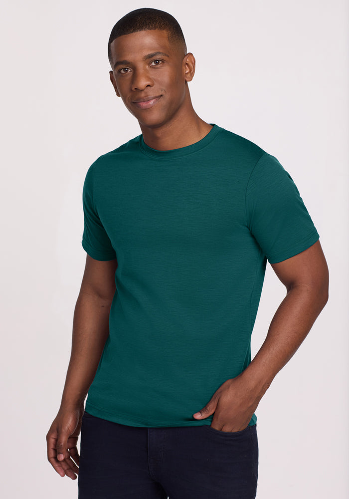 Man wearing a Woolx Endurance Tee in Riverbank Green and black pants, standing against a plain background, smiling.