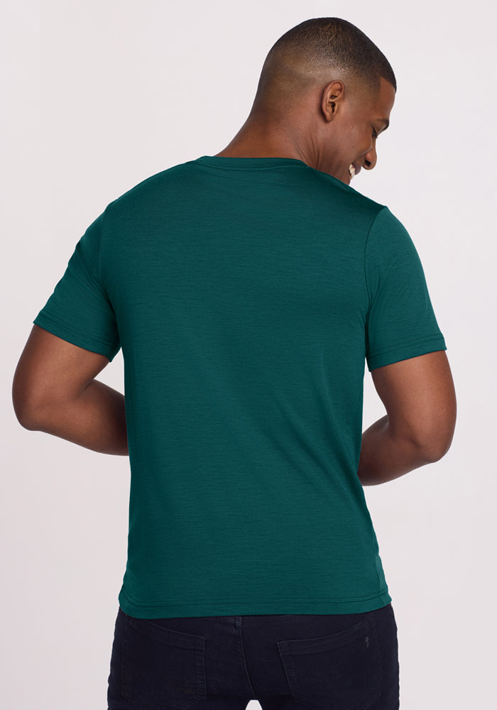 A man in a Woolx Endurance Tee in Riverbank Green is seen from the back, turning his head and smiling.