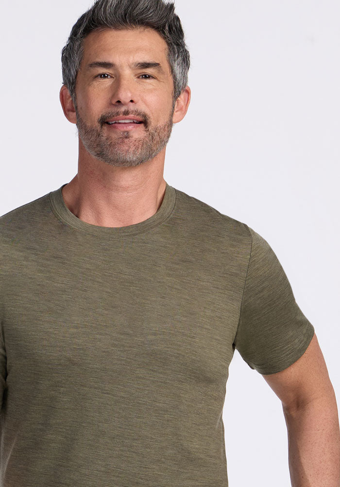 Man with salt-and-pepper hair in a Woolx Endurance Tee, Sage Olive Melange, smiles against a plain light background.