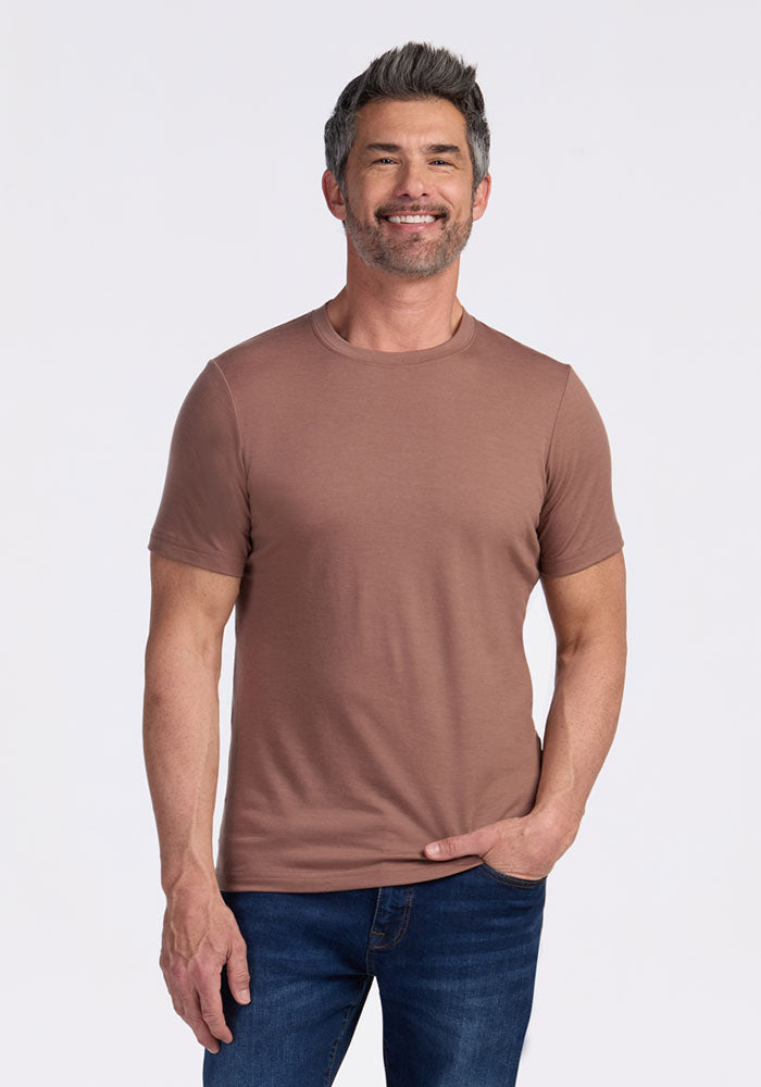 Smiling man in a Woolx Endurance Tee • Final Sale - Sienna Kiss and blue jeans, standing against a light background.