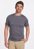 A person smiles while wearing a fitted Woolx Endurance Tee in Graphite Heather and beige pants, standing against a plain white background. They have short, dark hair with touches of gray and their right hand is in their pocket. | Matthew is 6’, wearing a size L