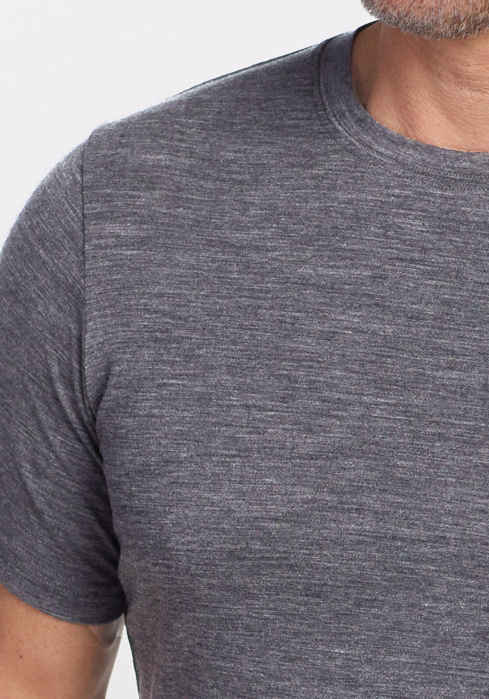 A close-up features a person wearing a Woolx Endurance Tee in Graphite Heather, capturing the upper torso and neck, elegantly highlighting the fabric's texture and performance quality.