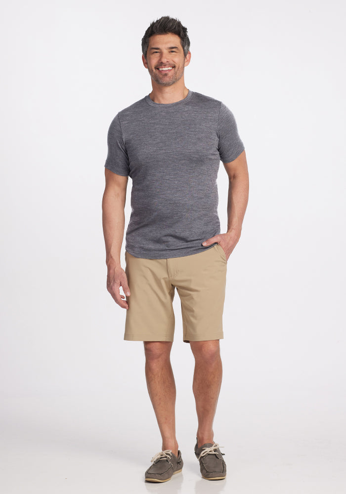 A man stands smiling, wearing a Woolx Endurance Tee in Graphite Heather and tan shorts, paired with brown boat shoes. With one hand in his pocket, he poses against a plain white background.