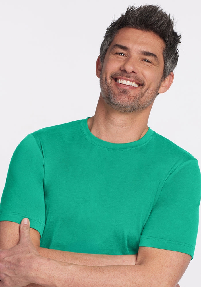 Smiling man wears the Woolx Endurance Tee - Jungle, arms crossed, in front of a light background.