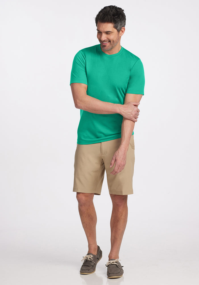 Man wears Woolx Endurance Tee - Jungle, beige shorts, and boat shoes, smiling with one arm bent against a white background.