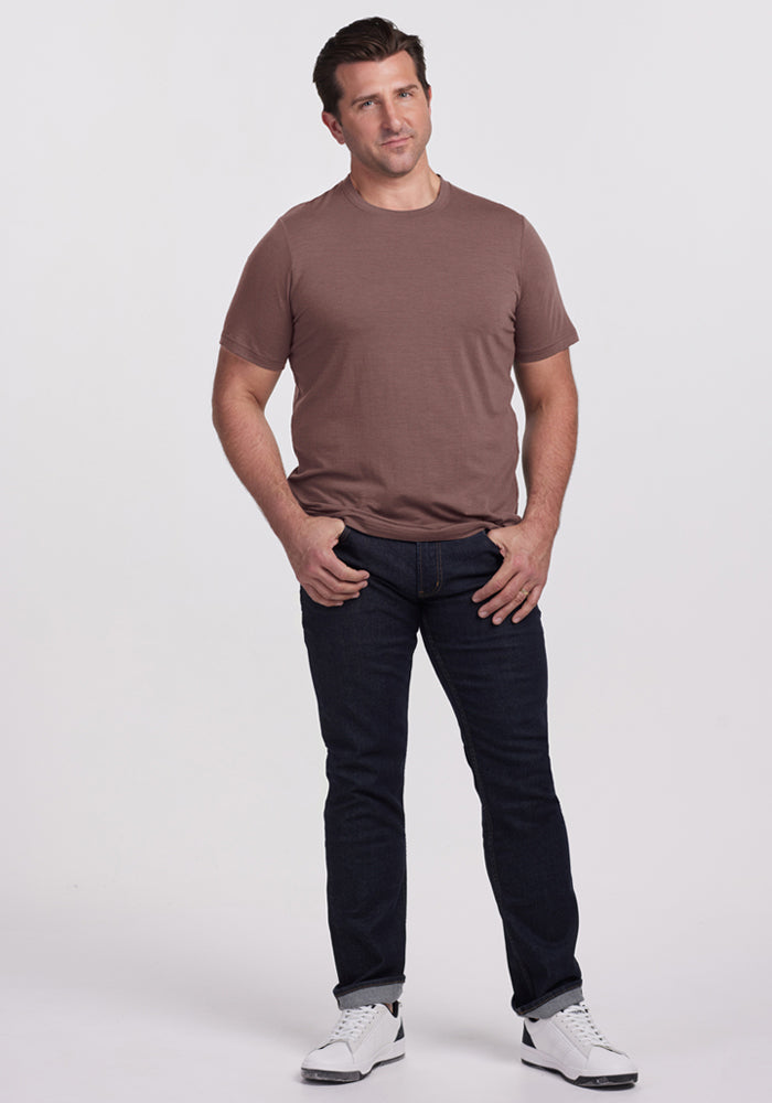 Man standing against a white background, wearing a Woolx Endurance Tee - Peppercorn, dark jeans, and white sneakers.