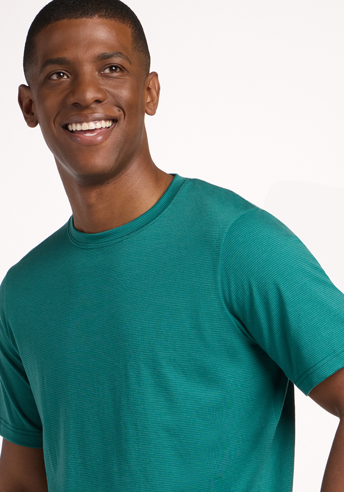 A smiling man wears the Woolx Endurance Tee - Woodland Mini Stripe, standing against a plain white background and looking slightly to the side.