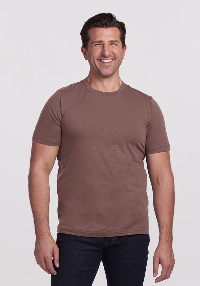 Smiling man in a Woolx Endurance Tee - Peppercorn and dark jeans stands against a plain light background. | Brandon is 6’3.5”, wearing a size XL